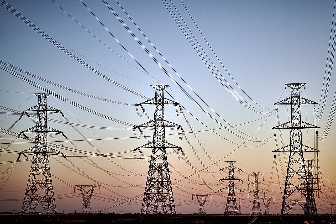 Electric transmission towers silhouetted against a sunset sky