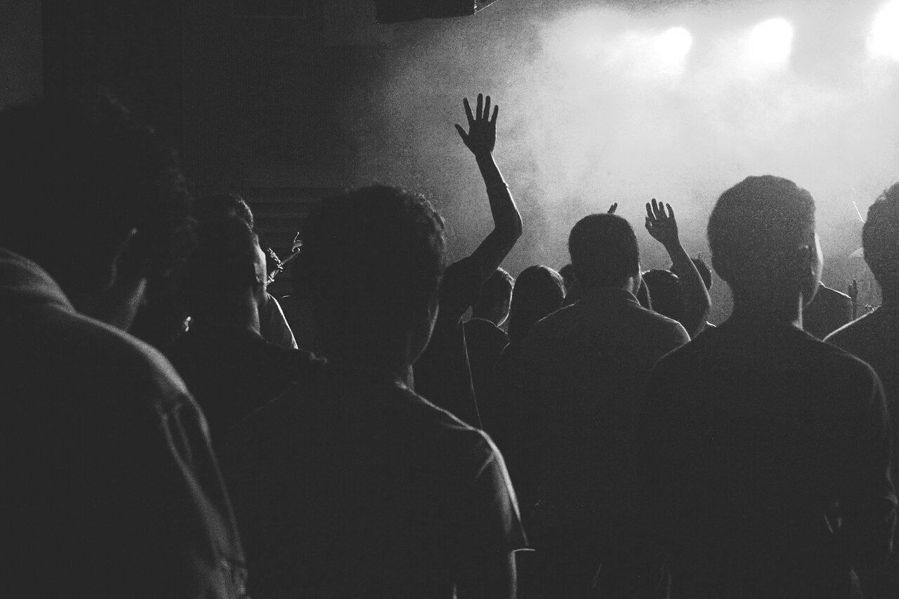Silhouetted concert crowd with hands raised under stage lights