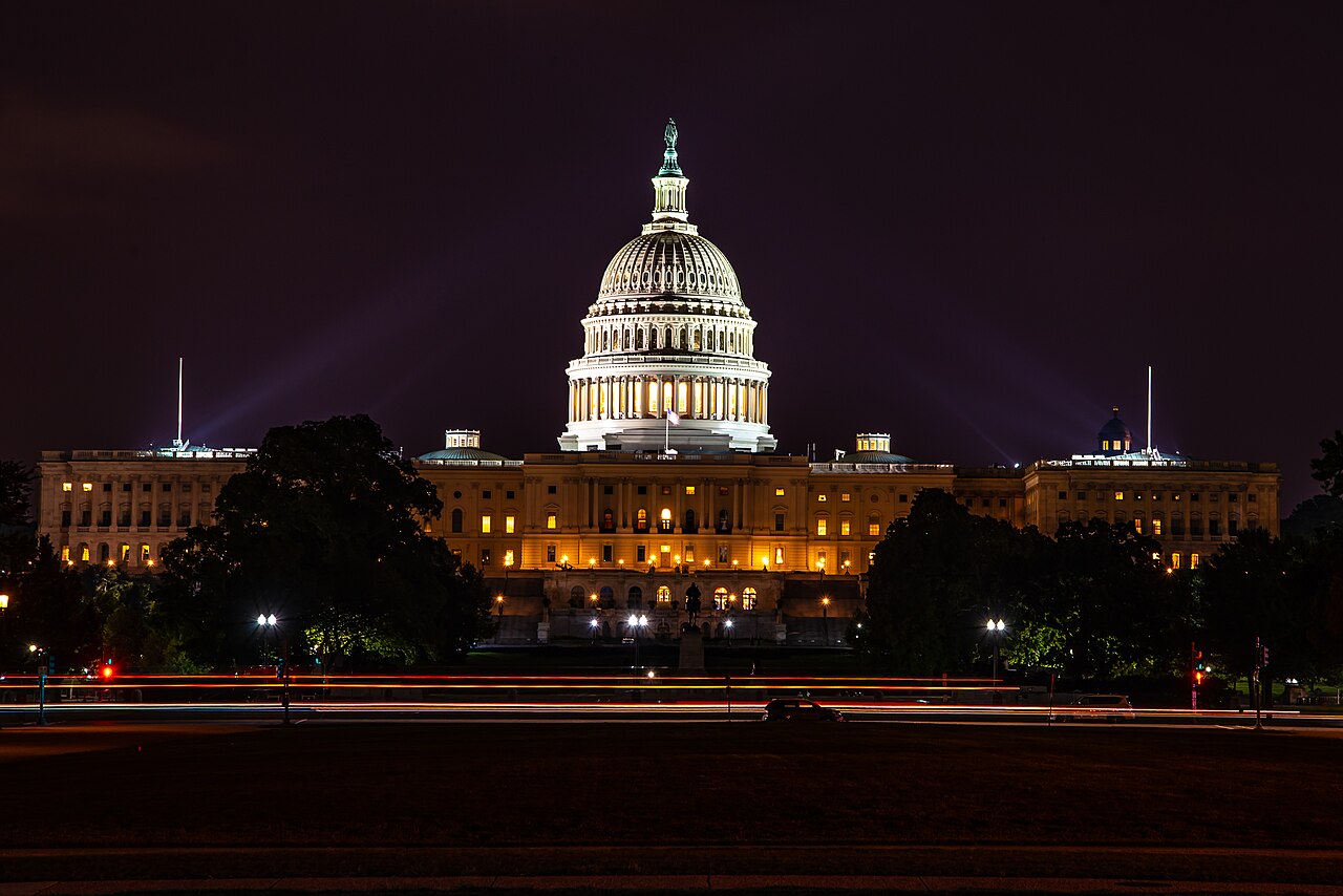 The U.S. Capitol illuminated at night, with light trails from traffic in the foreground