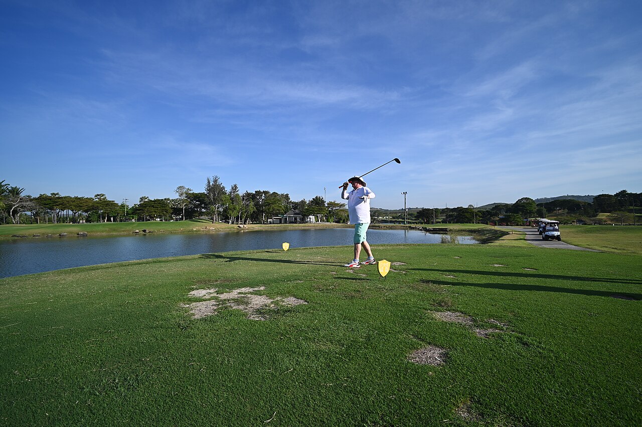 A golfer in mid-swing teeing off next to a water hazard on a sunny golf course