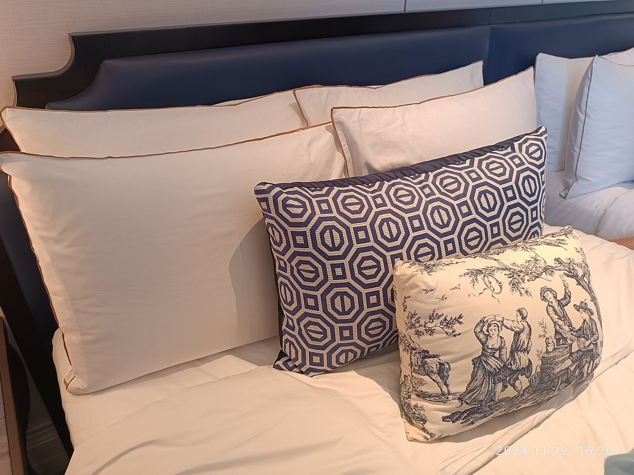 A hotel bed stacked with white and patterned pillows