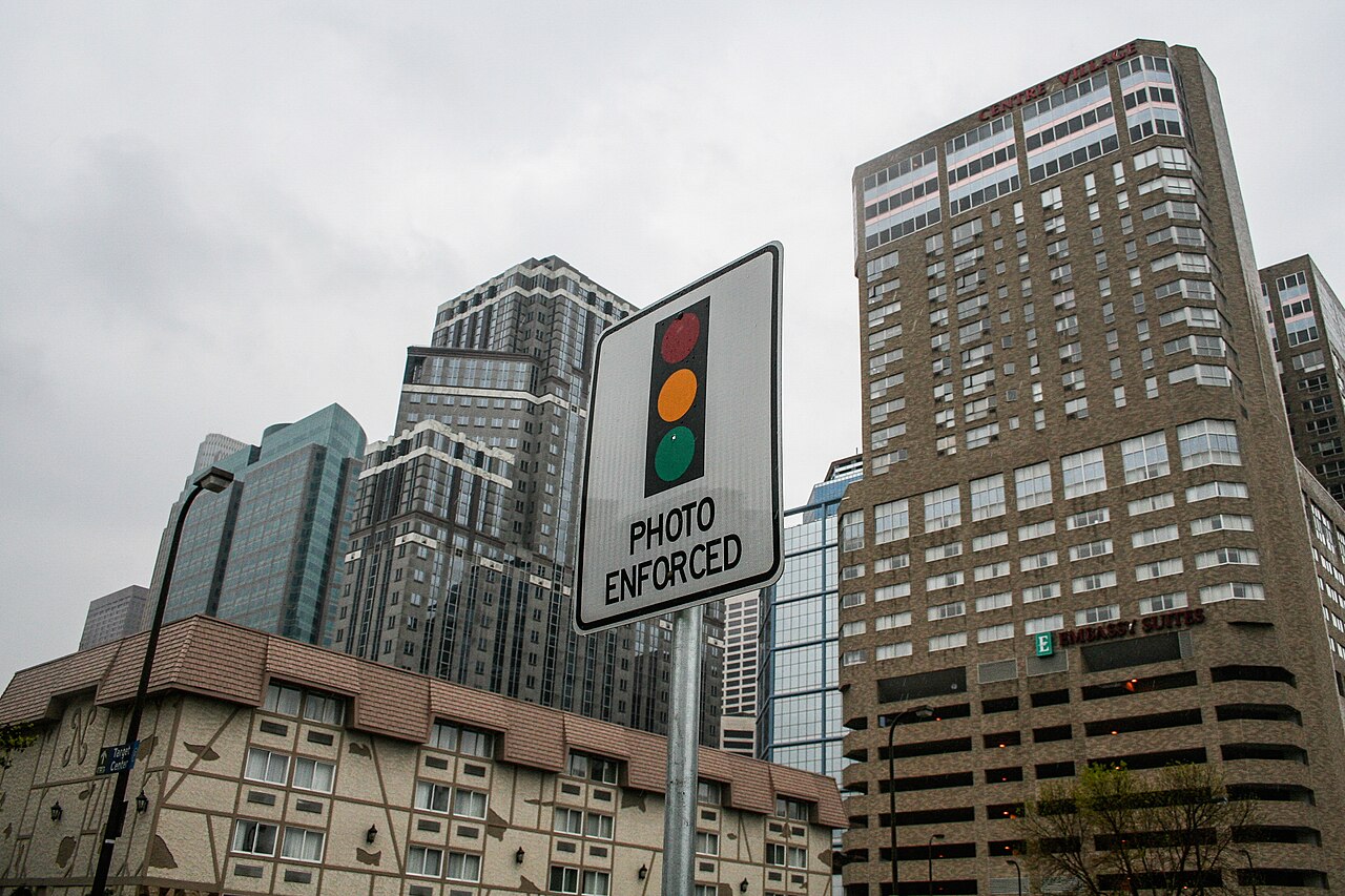 A photo enforced traffic light warning sign in front of downtown Minneapolis buildings