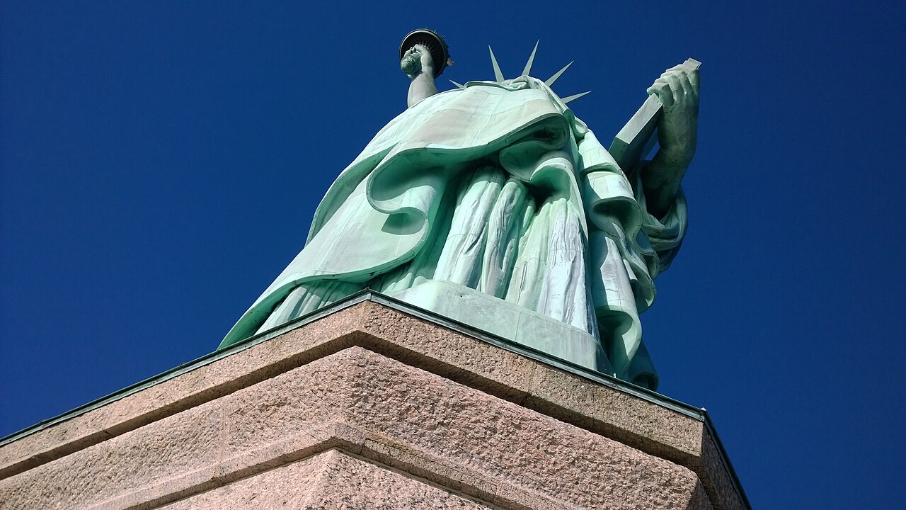 Statue of Liberty photographed from below, looking up at the pedestal and robes against a deep blue sky